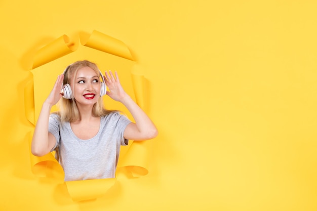 Young woman listening to music in headphones on a yellow surface