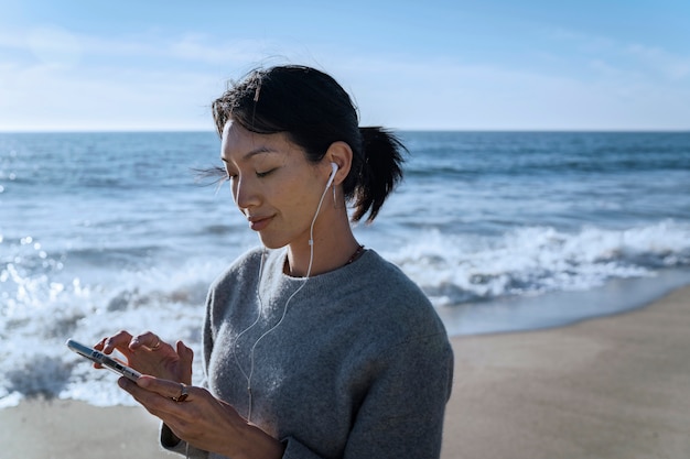 Young woman listening to music on smartphone at the beach using earphones