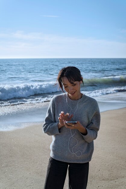 Молодая женщина слушает музыку на смартфоне на пляже в наушниках