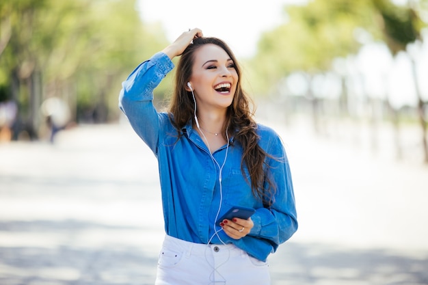 Foto gratuita giovane donna che ascolta la musica tramite le cuffie sulla strada estiva