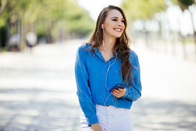 Молодая женщина слушает музыку через наушники на летней улице
