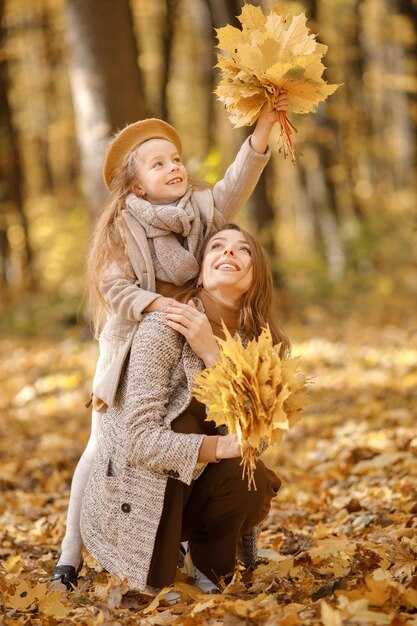 Young woman and little girl in autumn forest. Woman hugging her daughter. Girl wearing fashion clothes.