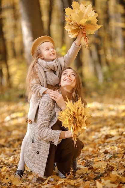 Young woman and little girl in autumn forest. Woman hugging her daughter. Girl wearing fashion clothes.