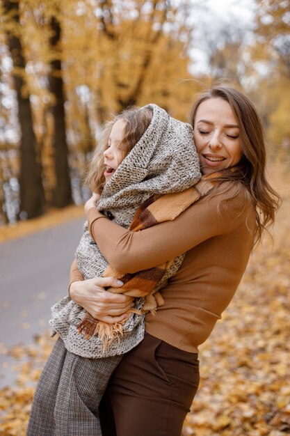 Young woman and little girl in autumn forest. Woman hugging her daughter. Girl wearing mother's oversize jacket.