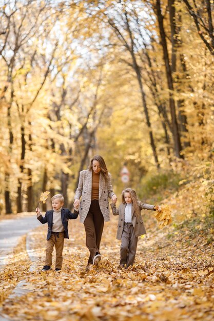 Молодая женщина, маленькая девочка и мальчик гуляют в осеннем лесу. Женщина, ее дочь и сын играют и веселятся. Девушка в модном сером костюме и мальчик в синей куртке.