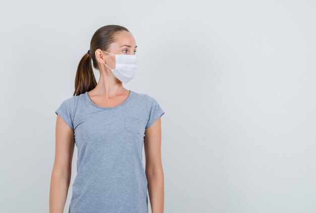 Young woman looking aside in grey t-shirt, mask , front view.