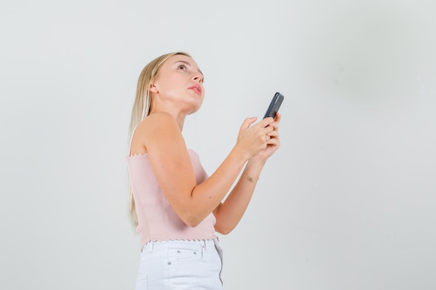 Young woman looking aside while holding smartphone in singlet