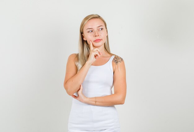 Young woman looking aside with finger on cheek in singlet