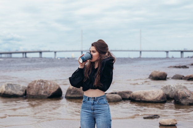Молодая женщина смотрит на море и пьет кофе