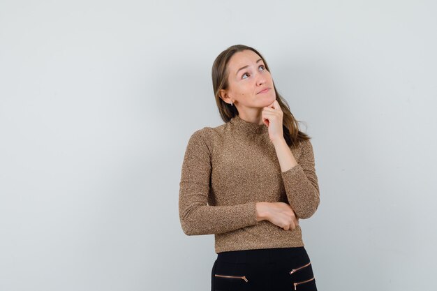 Young woman looking away in golden blouse and looking pensive