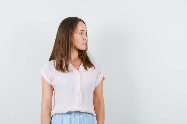 Young woman looking away in t-shirt, skirt and looking focused. front view.