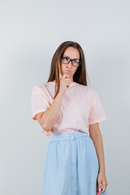 Young woman looking away in t-shirt, skirt and looking pensive. front view.