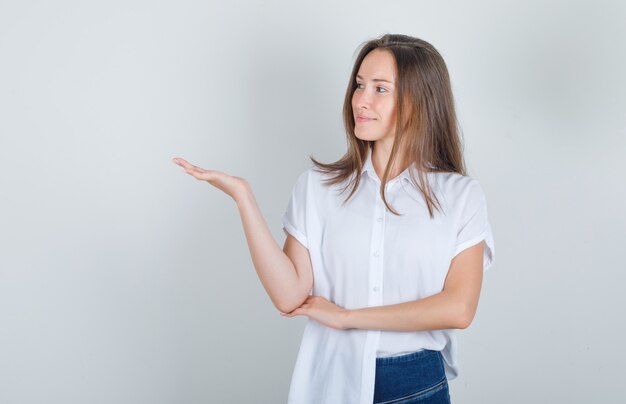 Young woman looking away with hand sign in white t-shirt, jeans and looking glad