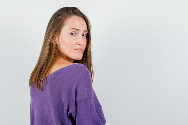 Giovane donna che guarda indietro in camicia viola e sembra ragionevole, vista posteriore.