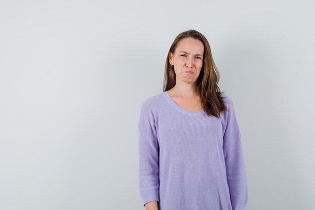 Young woman looking at camera in lilac blouse and looking unhappy 