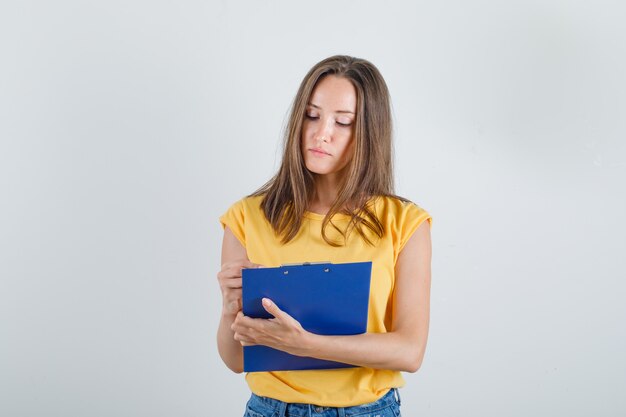 Молодая женщина смотрит в буфер обмена в футболке, шортах и выглядит занятой