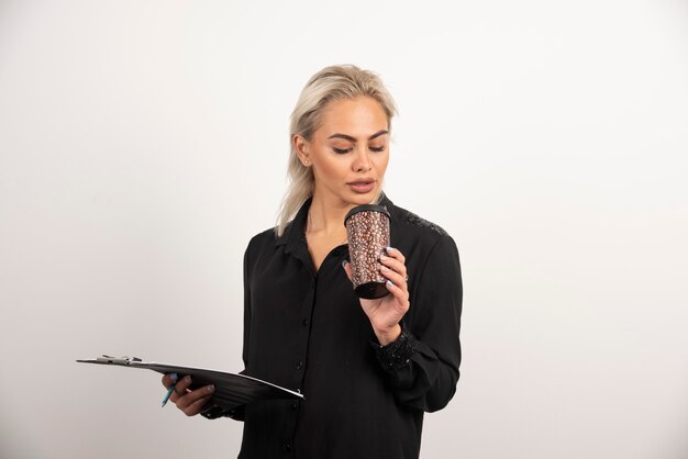 Young woman looking on a cup and holding clipboard on white background. High quality photo