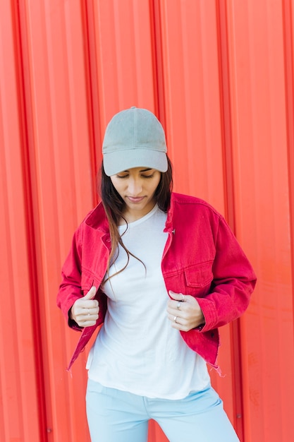 Free photo young woman looking down while holding red jacket standing against metal backdrop