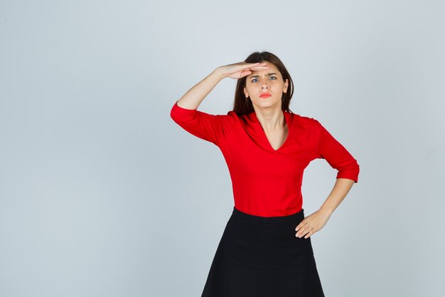 Young woman looking far away with hand over head, holding hand on hip in red blouse