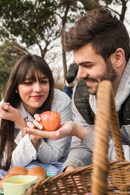 Young woman looking at fresh red apple hold by her boyfriend