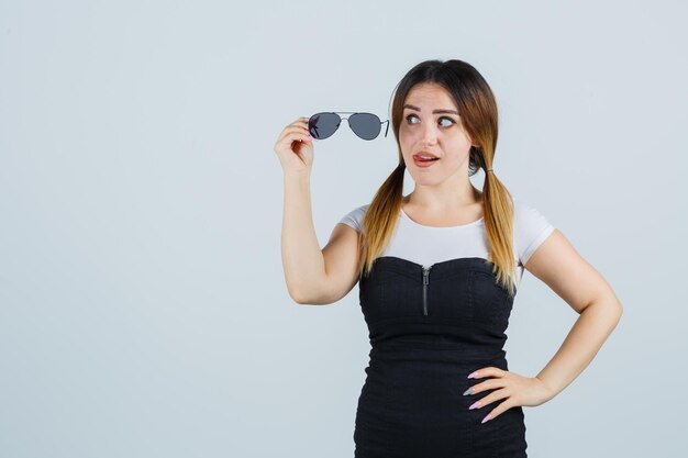 Young woman looking at glasses while keeping hand on hip