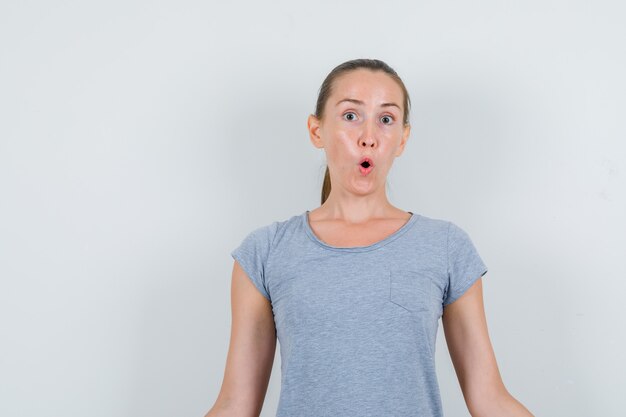 Young woman looking in grey t-shirt and looking surprised. front view.