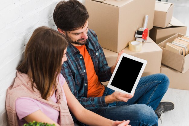 Young woman looking at her husband showing digital tablet