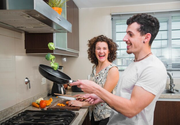 Young woman looking at her husband tossing broccoli in frying pan