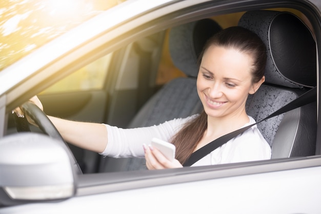 Young woman looking at her phone traveling by car