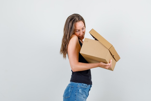 Young woman looking into cardboard box in singlet, shorts .