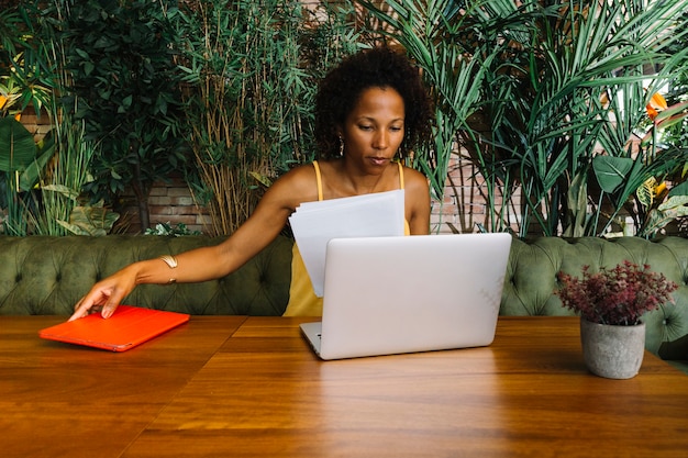 Free photo young woman looking at laptop holding document and digital tablet on wooden table