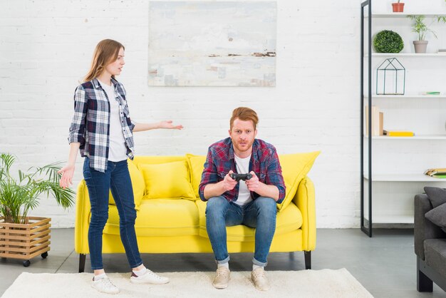 Young woman looking at man playing video game with joystick in the living room