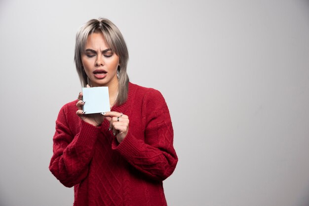 Young woman looking at memo pad on gray background.