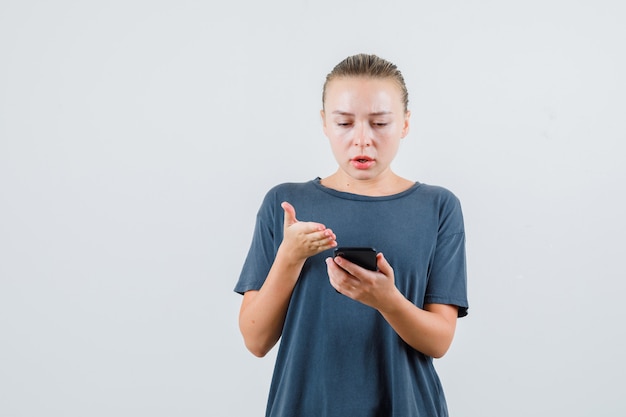 Young woman looking at mobile phone in grey t-shirt and looking confused