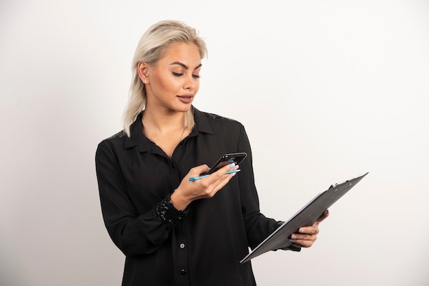 Young woman looking on mobile phone and holding a clipboard . High quality photo