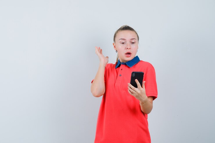 Free Photo young woman looking at mobile phone in t-shirt and looking surprised