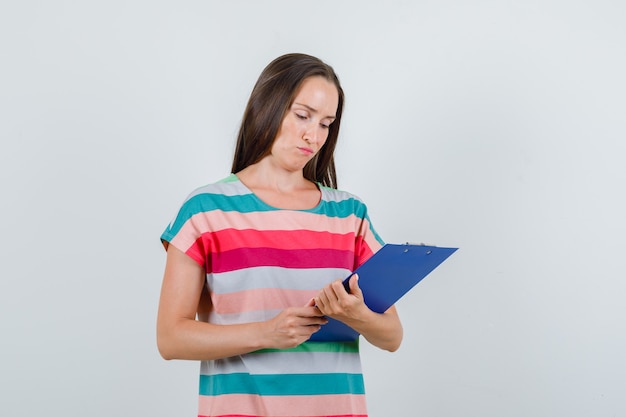 Young woman looking over notes on clipboard in t-shirt , front view.