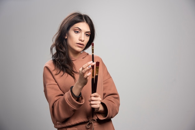 Young woman looking at paint brushes on gray