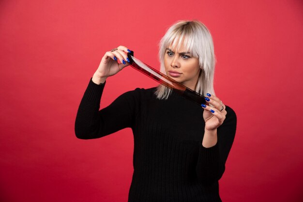 Young woman looking on a photo tape on a red background . High quality photo