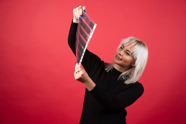 Young woman looking on a photo tape on a red background . High quality photo