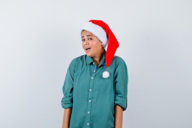 Young woman looking  in shirt, Santa hat and looking wondered , front view.