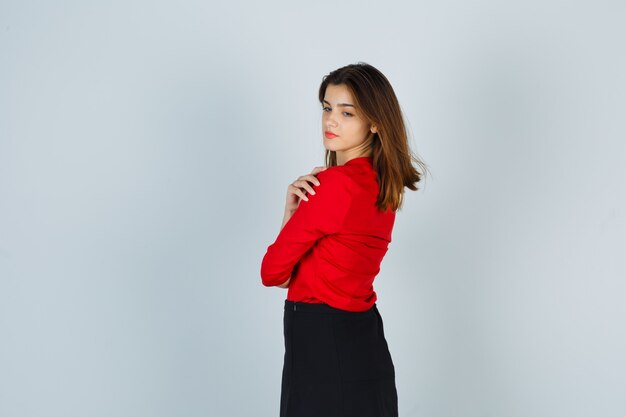 Молодая женщина смотрит через плечо в красной блузке, черной юбке и выглядит красиво