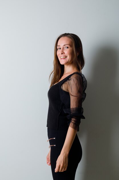 Young woman looking over shoulder and smiling gracefully in black blouse and black pants and looking charming