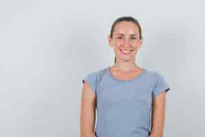 Foto gratuita giovane donna alla ricerca e sorridente in maglietta grigia, vista frontale.