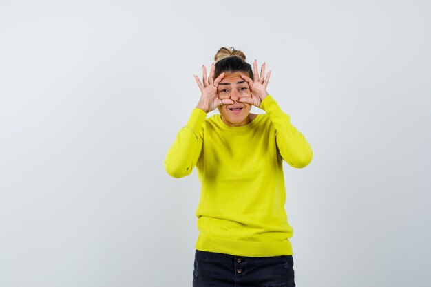 Young woman looking through fingers in yellow sweater and black pants and looking surprised