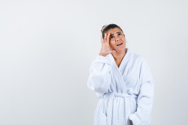 Young woman looking up in bathrobe and looking thoughtful