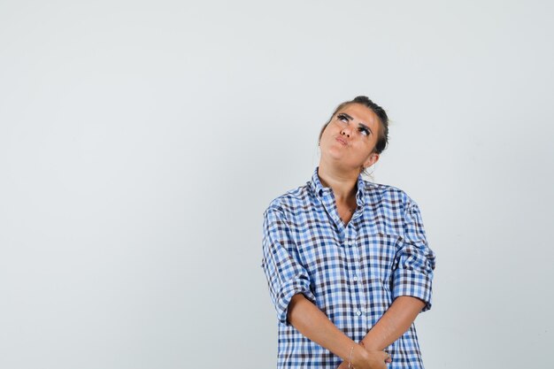 Young woman looking up in checkered shirt and looking pensive.