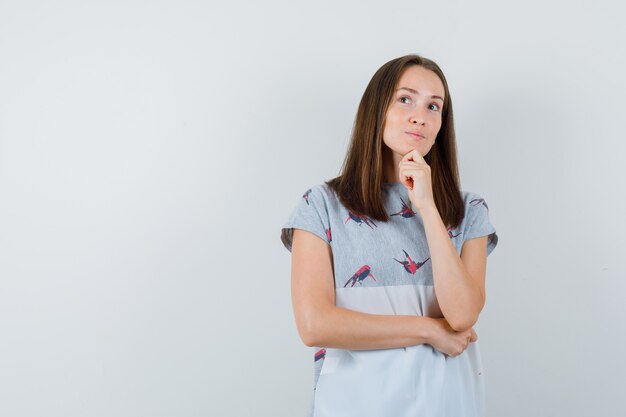 Young woman looking up in t-shirt and looking thoughtful , front view.