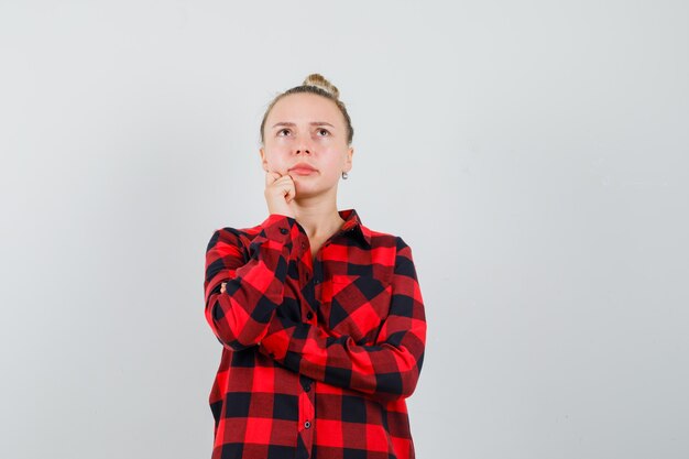 Free photo young woman looking up while thinking in checked shirt and looking doubtful