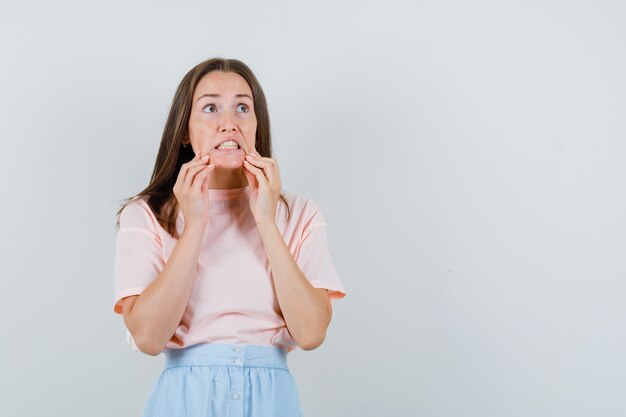 Young woman looking up with clenched teeth in t-shirt, skirt and looking scared. front view.